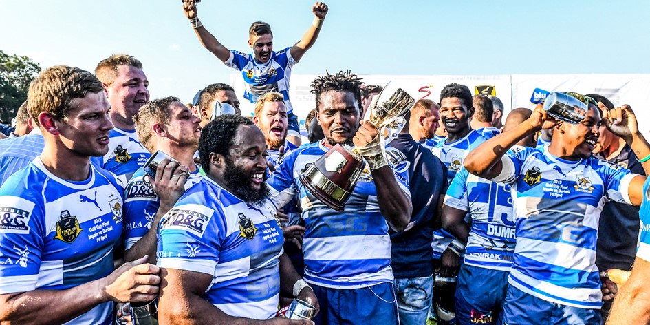Rustenburg Impala rugby team celebrates victory with trophy at the Gold Cup tournament, players in blue and white jerseys cheering and holding cups